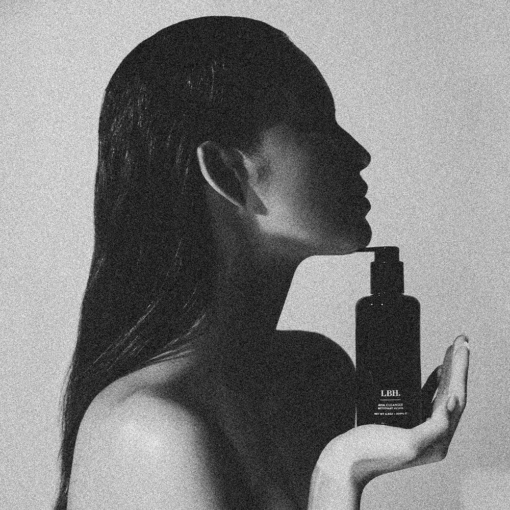 Model holding LBH Skincare AHA Cleanser black glass bottle